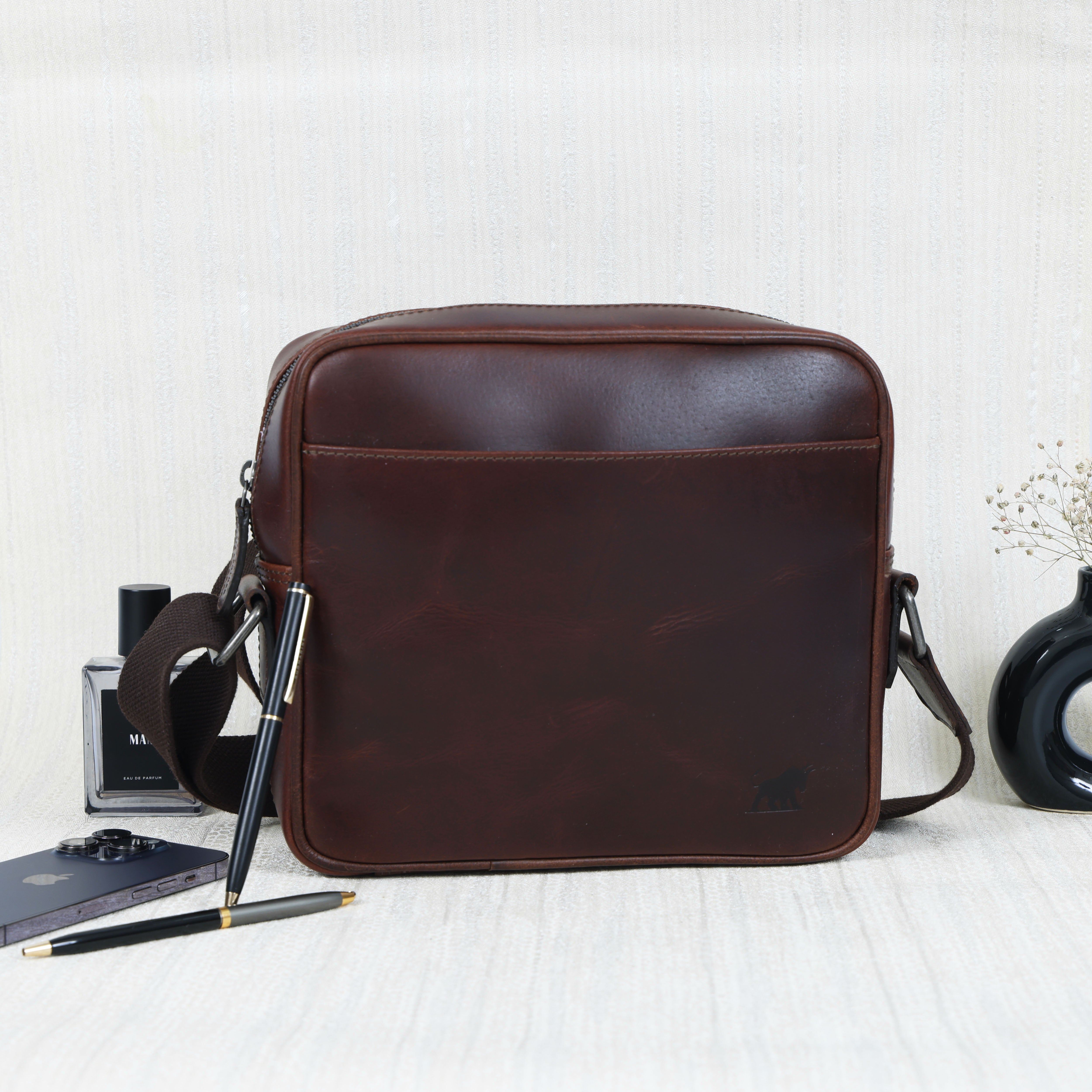 Premium Dark Brown Full-Grain Leather Cross-Body Bag from GM Leather Auckland displayed with a smartphone, perfume, and pens
