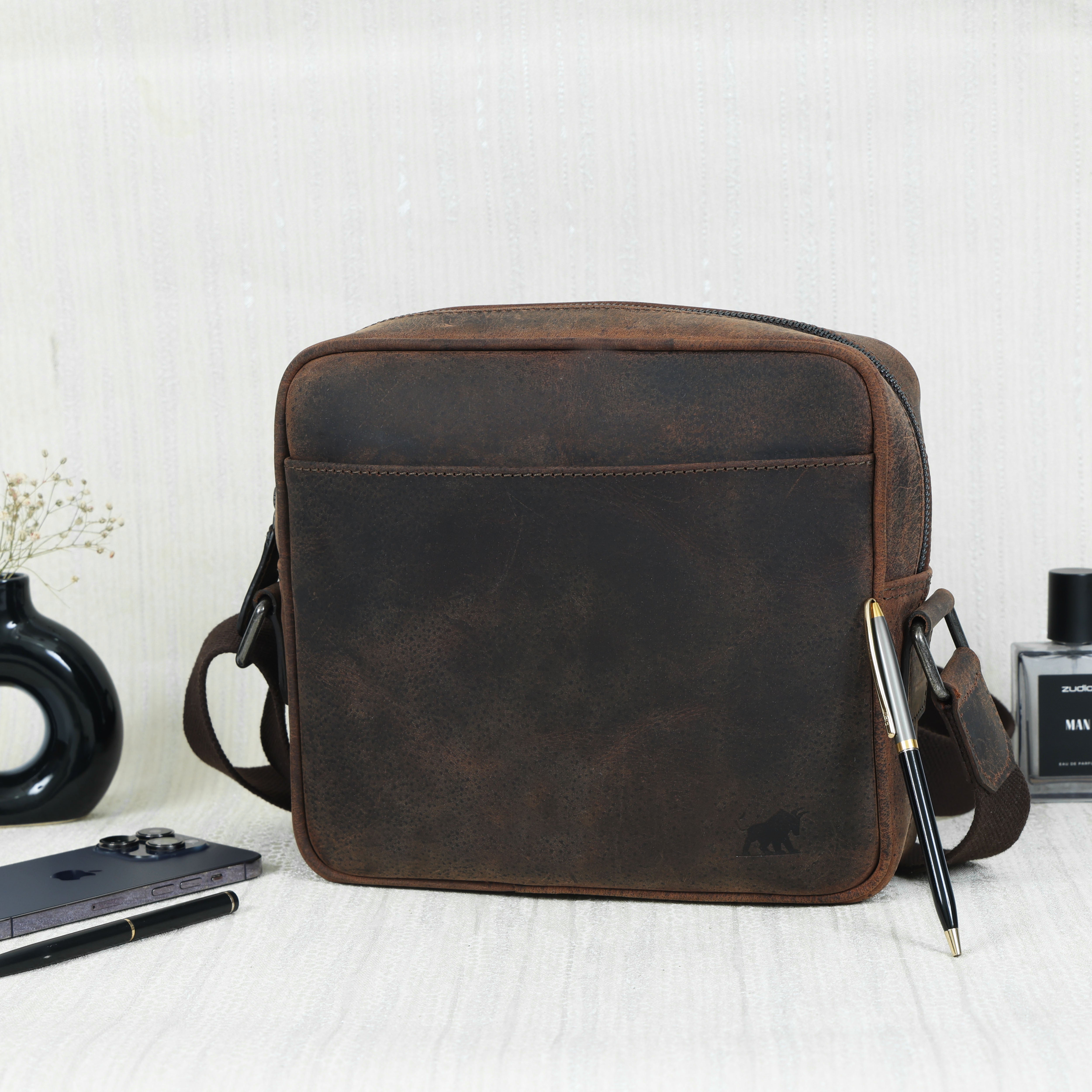 Premium Hunter Dark Brown Full-Grain Leather Cross-Body Bag from GM Leather Auckland displayed with a smartphone, perfume, and pens.