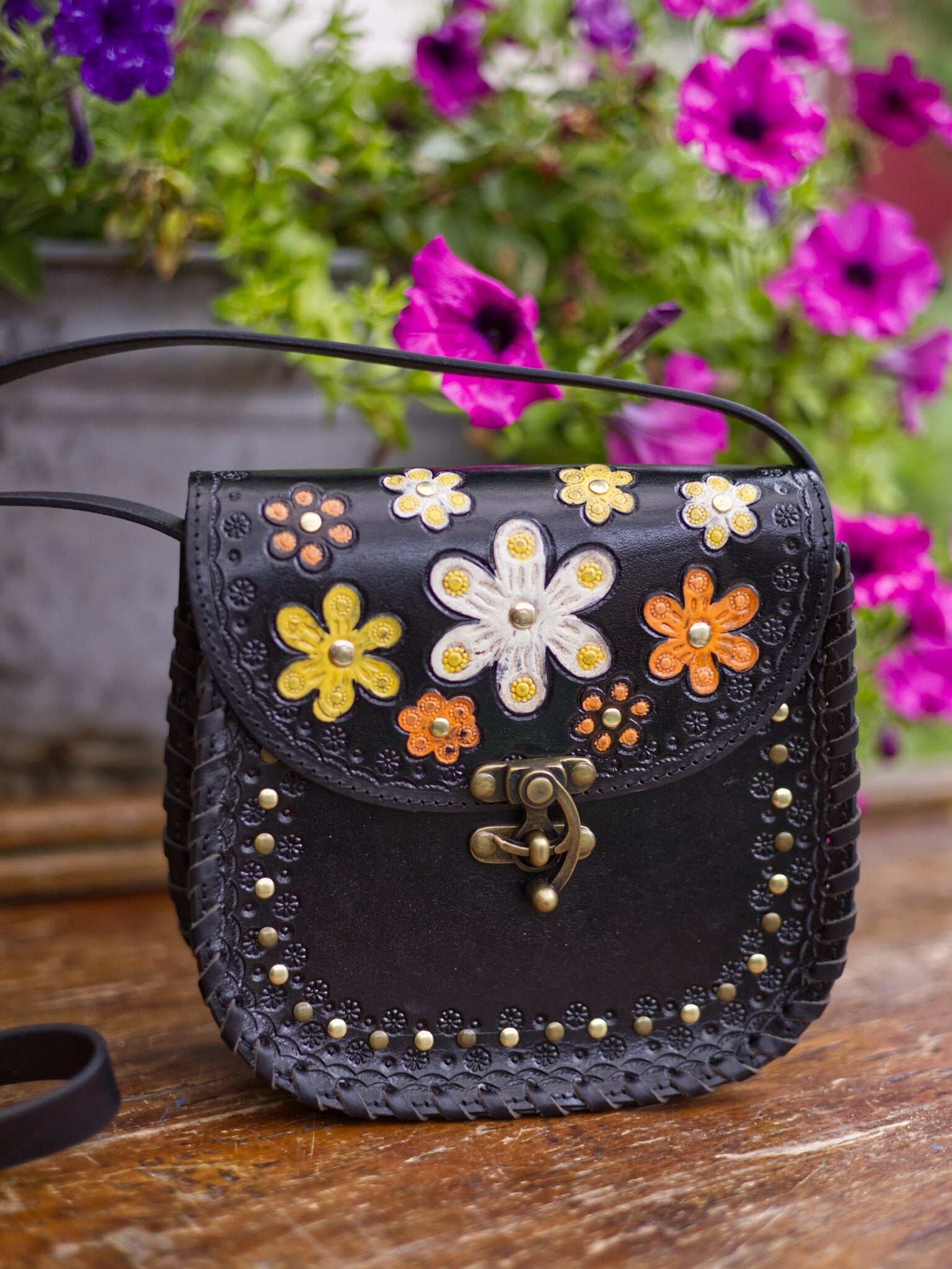Black handbag with floral designs on a wooden surface with flowers in the background